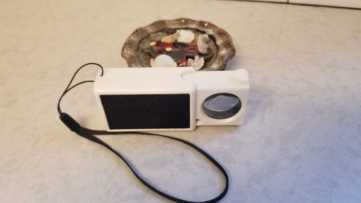 Small magnifier with wristband displayed with jewelry dish with geode pieces and other small trinkets perfect for enlarged viewing with magnifier. Available through NSC LLC. 