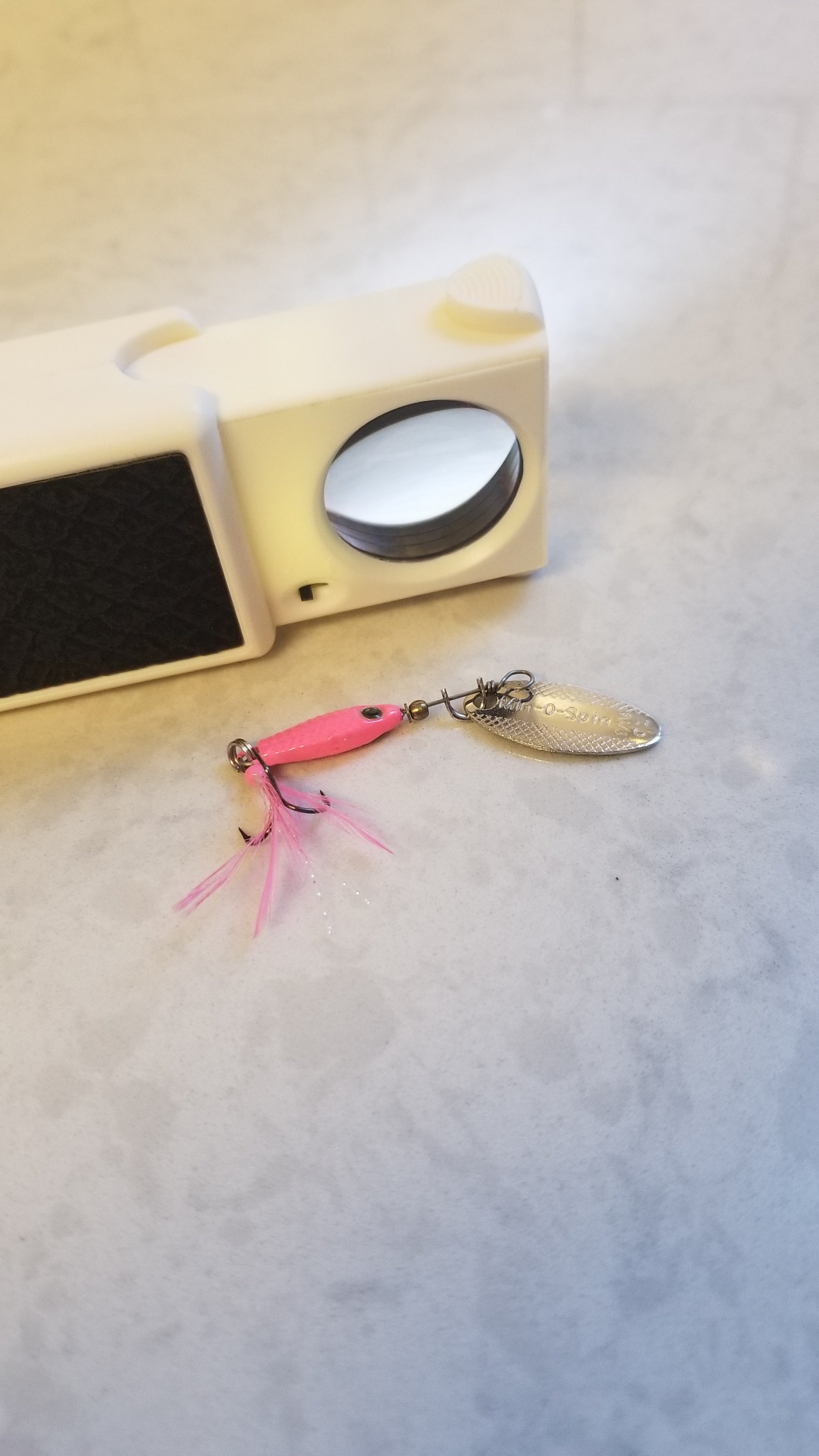 Magnifier with LED pulled out for use next to a fishing lure to suggest use for better visibility especially as a Bait & Tackle Tool or Bait & Tackle Gift.  Magnifier with Light Pocket Size available for purchase at National Supply Company LLC, an American company. 