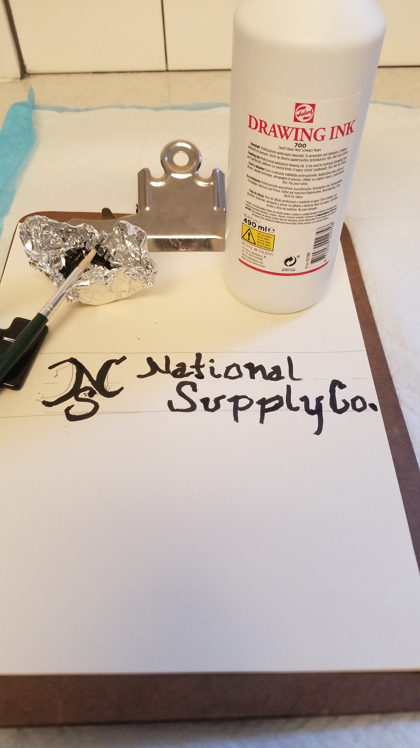 Drawing Ink Black 700 16 oz bottle on paper with artist's brush and ink supply to the left side. "NSC National Supply Co" is written in the ink to show quality of the traditional black ink. Available through National Supply Company LLC.